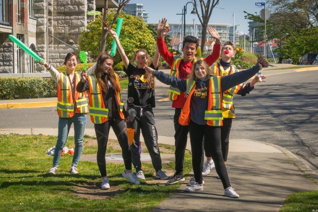 Young volunteers pose in vests, smiling and waving their hands.